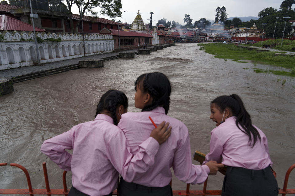 Tres niñas miran al río Bagmati, crecido por las lluvias del monzón, en Katmandú, Nepal, el miércoles 27 de julio de 2022. Un comité gubernamental que se creó para ayudar a limpiar el río estudia construir represas río arriba donde el agua de lluvia pueda capturarse y almacenarse durante la temporada del monzón y ser liberada durante los meses secos para descargar el río y mover los desechos río abajo desde Katmandú. (AP Foto/Niranjan Shrestha)