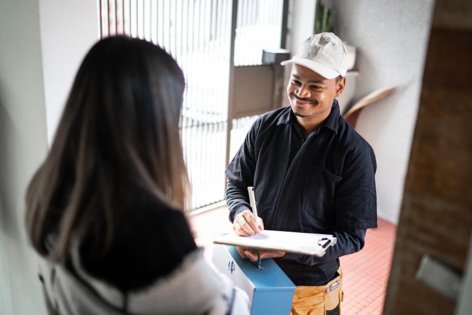 repairman-in-a-white-cap-holds-a-clipboard-and-a-pen-standing-in-the-doorway-talking-to-a-brunette-woman