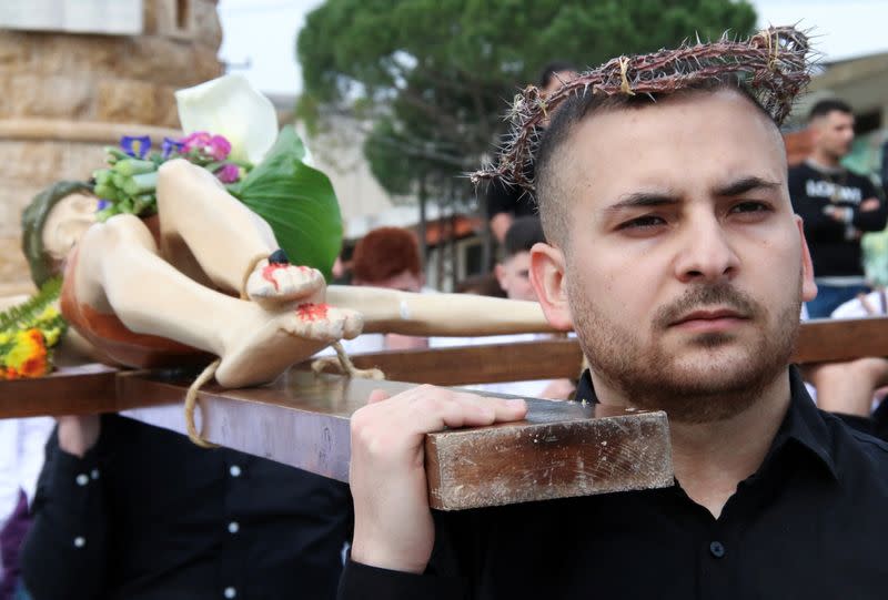 A christian worshipper takes part in the Good Friday procession as he carries a cross with a Jesus Christ statue, in the town of Klayaa