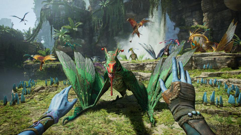 Two blue hands are shown from a first-person perspective. They appear to be trying to calm a dragon-like creature in Avatar: Frontiers of Pandora.