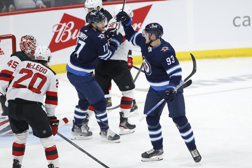 Winnipeg Jets' Kristian Vesalainen (93) and Adam Lowry (17) celebrate Vesalainen's goal against New Jersey Devils goaltender Jonathan Bernier (45) during the first period of an NHL hockey game Friday, Dec. 3, 2021, in Winnipeg, Manitoba. (John Woods/The Canadian Press via AP)