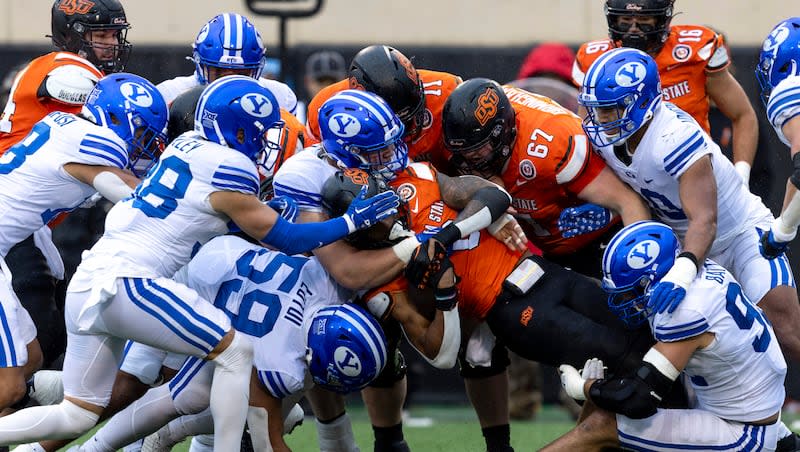 BYU defensive end Logan Lutui, left, defensive tackle Bruce Mitchell, center, and defensive end Tyler Batty, right, tackle Oklahoma State running back Ollie Gordon II (0) in the first half of an NCAA college football game Saturday, Nov. 25, 2023, in Stillwater, Okla.