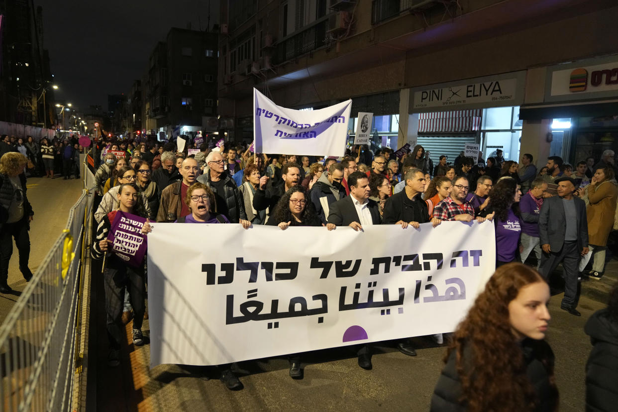 Israeli lawmakers Ayman Odeh, center right, Mossi Raz, second from right, and Ofer Cassif, right, march behind a banner reading "This is our home. This is our home," in Tel Aviv, Israel, to protest against Prime Minister Benjamin Netanyahu's far-right government, Saturday, Jan. 7, 2023. (AP Photo/ Tsafrir Abayov)