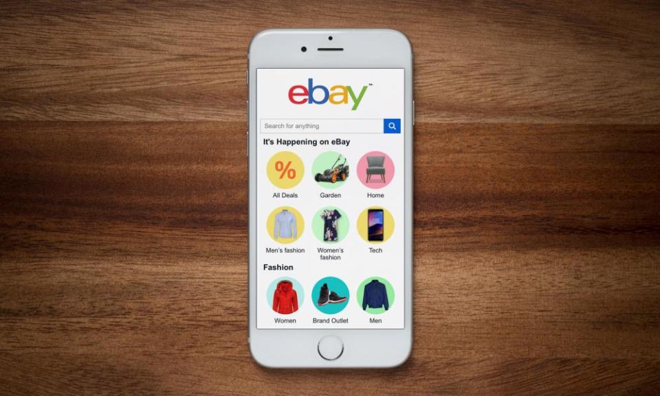 An iPhone showing the ebay website rests on a plain wooden table.