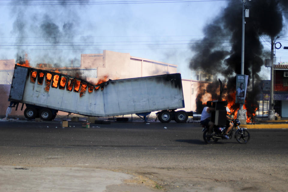 Men ride on a motorcycle past a burning truck on the streets of Culiacan, Sinaloa state, Thursday, Jan. 5, 2023. Mexican security forces have captured Ovidio Guzmán, an alleged drug trafficker wanted by the United States and one of the sons of former Sinaloa cartel boss Joaquín "El Chapo" Guzmán, in a pre-dawn operation outside Culiacan which has caused a wave of violence in the city. (AP Photo/Martin Urista)