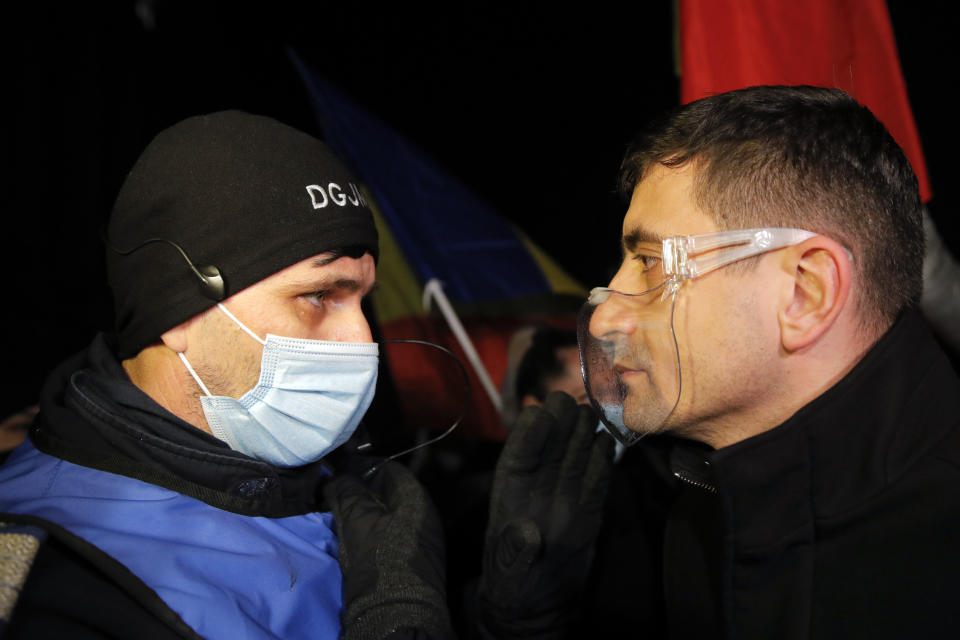 George Simion, one of the leaders of the Alliance for the Unity of Romanians or AUR, speaks to a gendarme during a protest outside the health ministry after a deadly fire at a hospital treating COVID-19 patients in Bucharest, Romania, Saturday, Jan. 30, 2021. Hundreds marched during a protest organized by the AUR alliance demanding the resignation of several top officials, after a fire early Friday at a key hospital in Bucharest that also treats COVID-19 patients killed five people. (AP Photo/Vadim Ghirda)