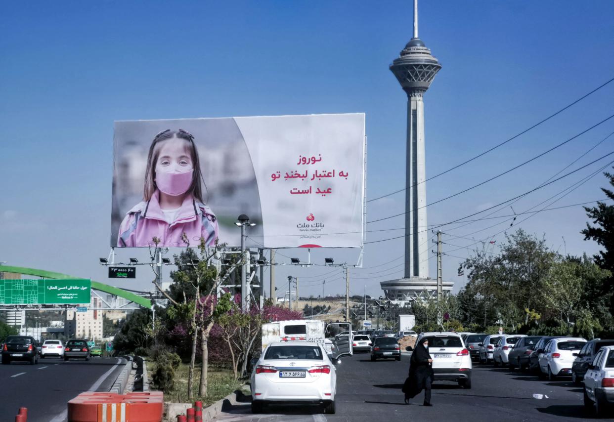 A woman wearing a protective mask amid the coronairus pandemic crosses an avenue in Iran's capital Tehran with a view of Milad Tower, on April 5, 2021.