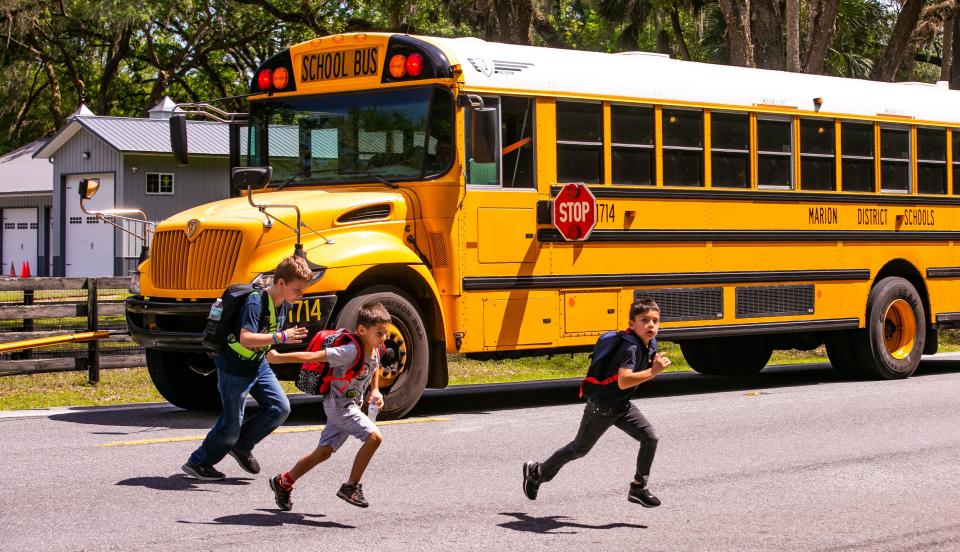 Shady Hill Elementary School students Samuel Powell, 10, left, Christian Carrera, 6, center, and his brother Roman Carrera, 8, sprint across south Magnolia Avenue in front of their school bus at their drop off at Southwest 84th Street on Wednesday.