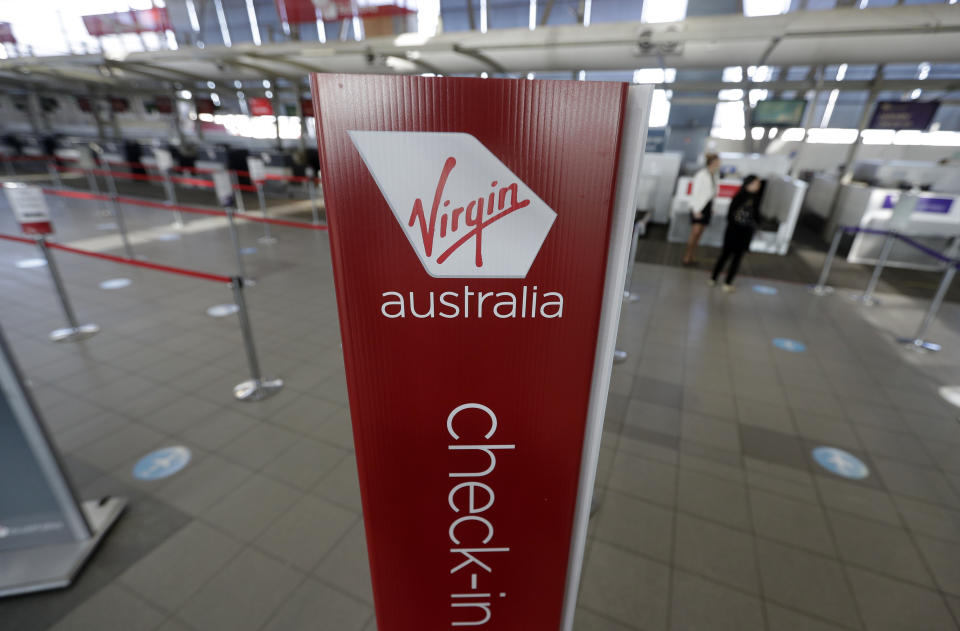 A sign is displayed at empty check-in counters for Virgin Australia at Sydney Airport in Sydney, Wednesday, Aug. 5, 2020. Virgin Australia will cut about 3000 jobs as the airline struggles with the effects of the coronavirus pandemic. (AP Photo/Rick Rycroft)