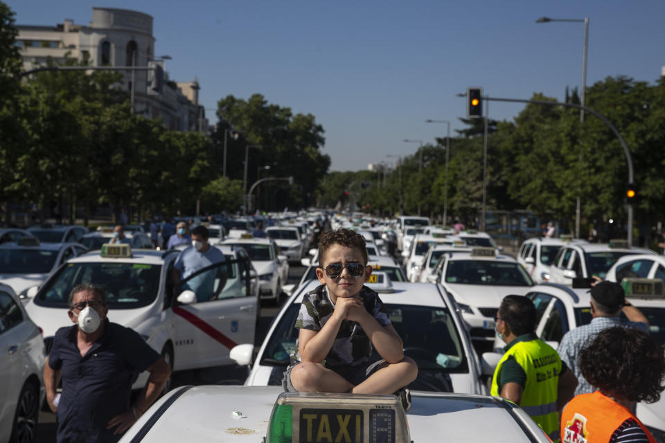 A child sits on the roof of a taxi during a taxi driver protest in downtown Madrid, Spain, Tuesday, June 30, 2020. Taxi drivers are demanding assistance due to lack of clients and private hire. (AP Photo/Manu Fernandez)