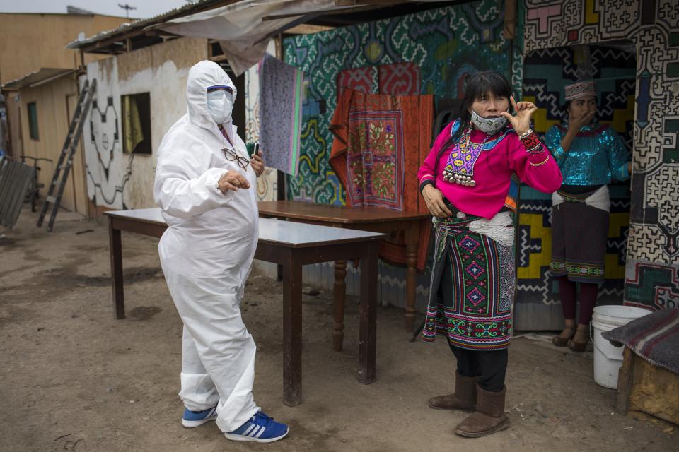 Olinda Silvano from the Shipibo Conibo ethnic group, talks to a member of an NGO dressed in protective gear against the new coronavirus, during the celebration of the feast of Saint John the Baptist, the patron saint of the Peruvian Amazon, in the Cantagallo neighborhood of Lima, Peru, Wednesday, June 24, 2020. The neighborhood reopened about 10 days ago after it had been under strict quarantine due to an outbreak of COVID-19. (AP Photo/Rodrigo Abd)