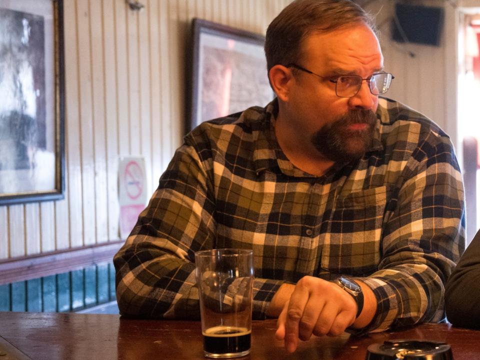 greg larsen as ethan krum in the tourist. he's wearing a flannel shirt, with a half drunk dark beer in front of him