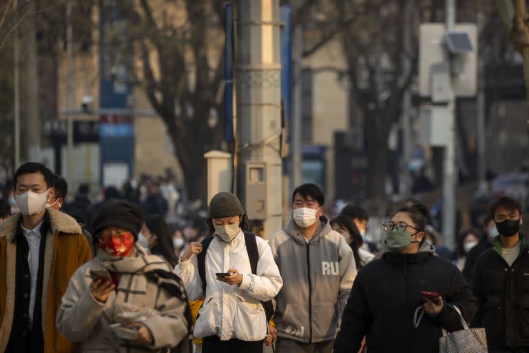 Personas con mascarillas caminan por una calle durante la hora pico de la mañana en el distrito comercial central de Pekín