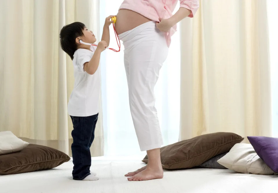 toddler using a stethoscope to try to listen to his pregnant mom's belly