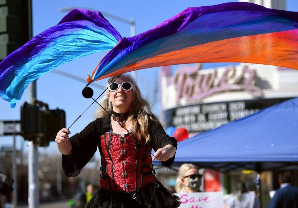 Tammy Eggert hace girar pancartas mientras se para sobre zancos. Más de 100 personas se reunieron en un ambiente de carnaval frente al Tower Theatre para protestar contra la rezonificación y la compra del teatro por Adventure Church la mañana del domingo, 21 de febrero de 2021, en Fresno.