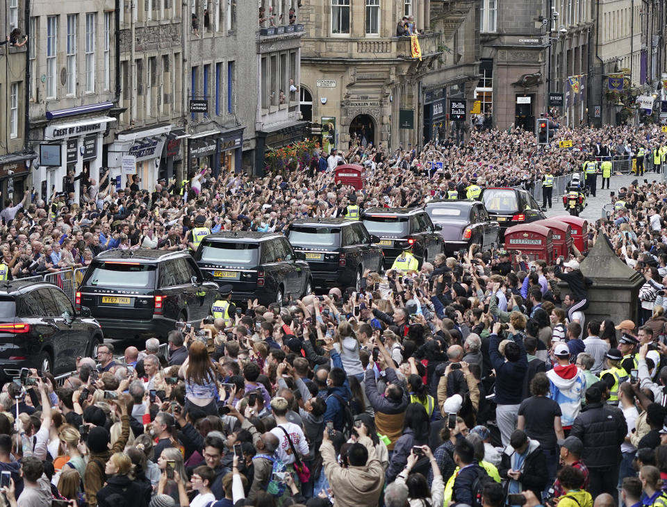 Crowds watch as the hearse carrying the coffin of Queen Elizabeth II, draped with the Royal Standard of Scotland, passes Mercat Cross in Edinburgh, Sunday, Sept. 11, 2022, as it continues its journey to the Palace of Holyroodhouse from Balmoral. (Ian Forsyth/Pool Photo via AP)