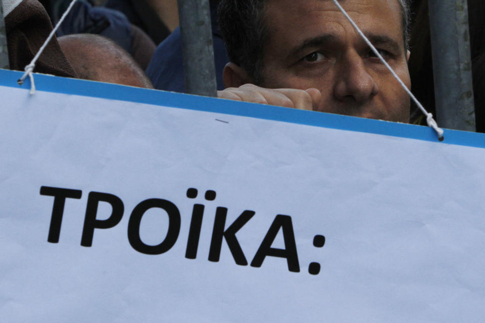 A protestor is seen behind a banner that reads in Greek "Troika" on a barricade outside of Parliament during a strike to protest government plans to privatize the state-run organizations in Nicosia, Cyprus, Thursday, Feb. 27, 2014. Hundreds of protesters have gathered outside Cyprus' parliament to voice opposition against legislation that will pave the way for the privatization of state-owned companies. (AP Photo/Petros Karadjias)