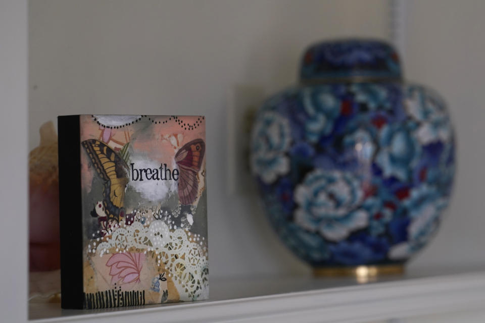 A wall hanging with the message "Breathe" given to Keri Wegg by her sister, Kelly Garcia, after Keri's rehabilitation from a double-lung transplant, sits on a shelf in her in Westfield, Ind., home on Monday, March 22, 2021, next to the urn containing the ashes of Keri's father, Gladin Fleming. (AP Photo/Charles Rex Arbogast)