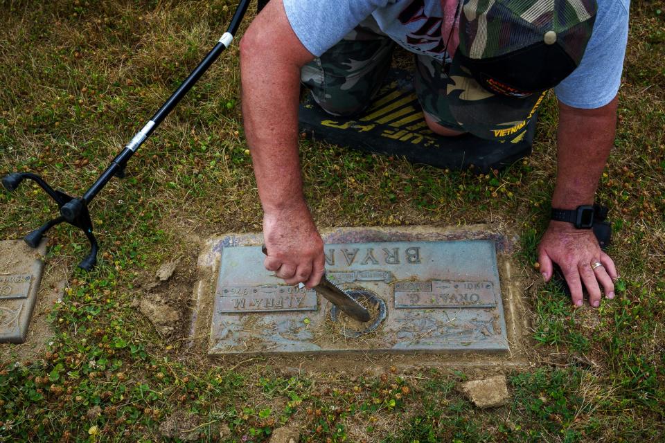 With a garden tool, Rick Brown removes dirt from a vase hole cover Thursday, July 7, 2022, inside Forest Lawn Memory Gardens in Greenwood. Brown, Indiana point man for the nationwide non-profit Mission Restore Bronze, helps restore and clean grave markers of veterans who have died. The service is done at no cost to the family. Brown is a veteran himself, serving two tours in Vietnam. He's disabled now. He says it's most likely a mixture of Agent Orange, a traffic accident breaking his leg after his first tour in Vietnam, and now Parkinson's disease, but says he's happy to be off pain killers. 