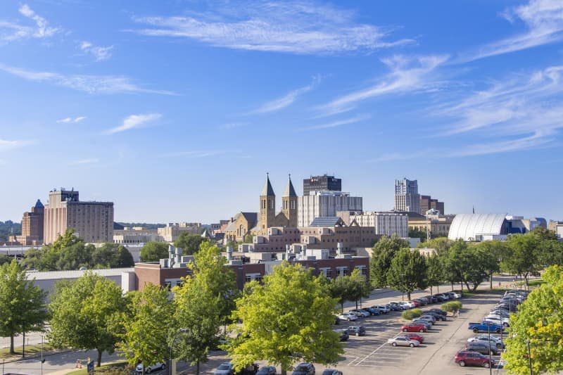 This elevated view of downtown Akron Ohio shows how developed the city has become. A mix of old and new architecture, the city stands beyond some scattered trees under a predominately blue sky.