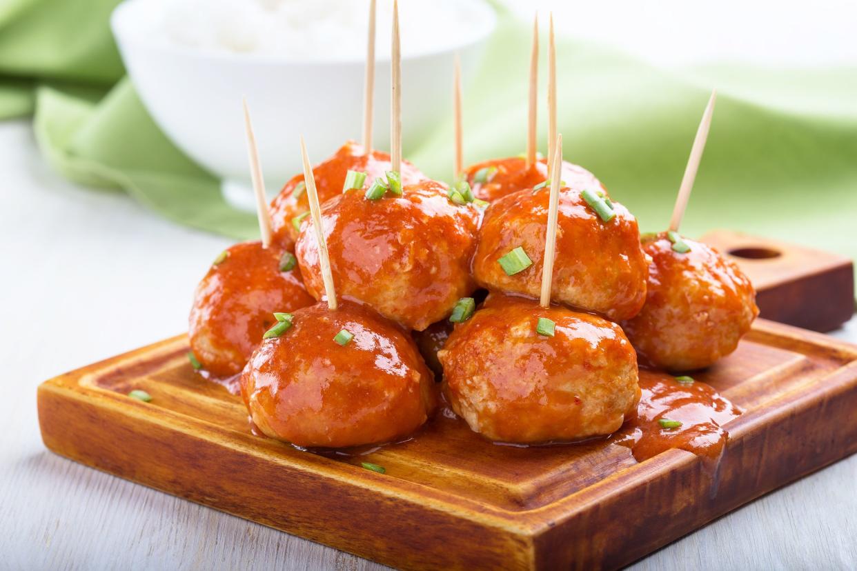 Slow cooker firecracker chicken meatballs with toothpicks on a wooden cutting board with a blurred background of a white bowl and an olive green cloth