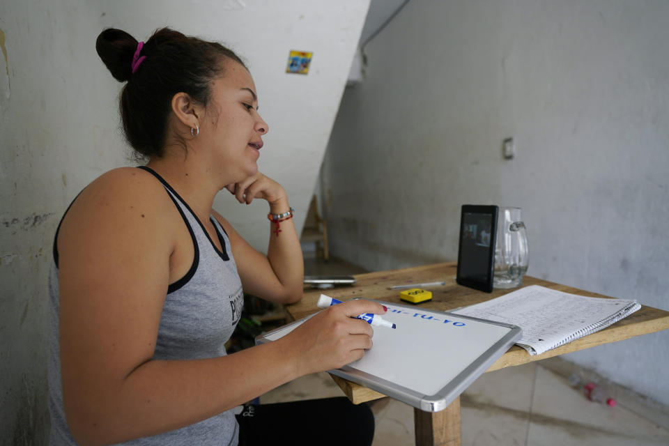 Gabriela Fajardo, a 26-year-old Honduran seeking asylum in the United States, teaches a Zoom class for Central American children living in camps, various shelters and apartments in other parts of Mexico from a hallway of an aged building in Matamoros, Mexico, on Friday, Nov. 20, 2020. Like countless schools, the sidewalk school went to virtual learning amid the coronavirus pandemic but instead of being hampered by the change, it has blossomed. (AP Photo/Eric Gay)