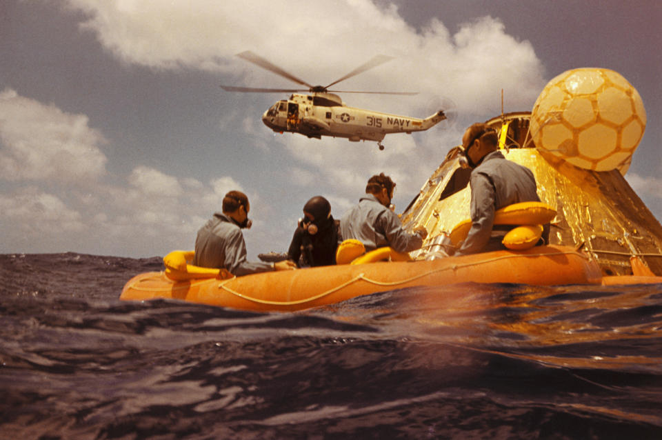 (Original Caption) In The Pacific Ocean - Apollo 12 astronauts, assisted by a Navy swimmer, (2nd from left), sit in their raft awaiting a helicopter pickup by Navy helicopter (above), after a successful splashdown in the ?Command Module. Left to right: Alan Bean, swimmer, Richard Gordon, and Charles Conrad. (NASA)