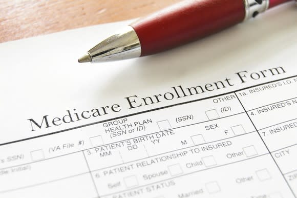 Medicare enrollment form on a wood desk with a red pen on top of the form.