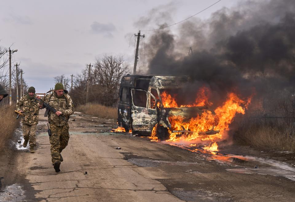 Ukrainian soldiers pass by a volunteer bus burning after a Russian drone hit it near Bakhmut.