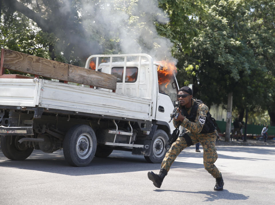 A Presidential Guard runs with his weapon drawn next to his unit's burning truck during clashes with mourners and demonstrators who were carrying the coffins with the remains of two victims of the ongoing violence, near the Presidential Palace in Port-au-Prince, Haiti, Wednesday, Oct. 16, 2019. At last two people were injured in the clashes the while thousands across Haiti attended funerals for protesters who have died in ongoing demonstrations aimed at ousting President Jovenel Moise. (AP Photo/Rebecca Blackwell)