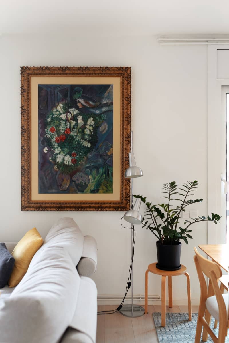 White living room wall with large framed artwork next to a silver lamp and plant.