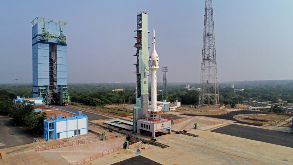 a white rocket sits atop a launch pad, with green trees in the background.