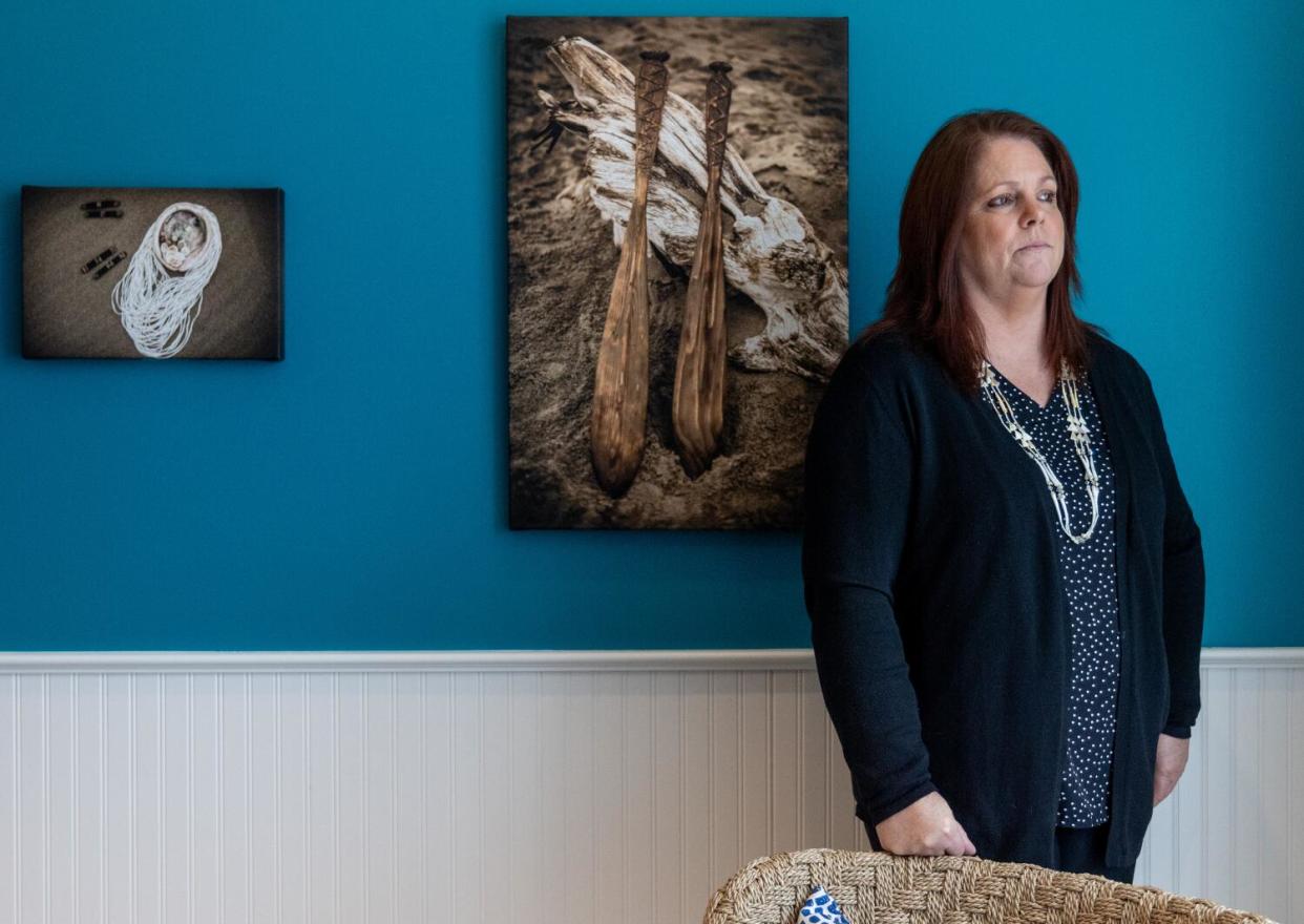 A woman stands next to tribal art hung on a blue wall.