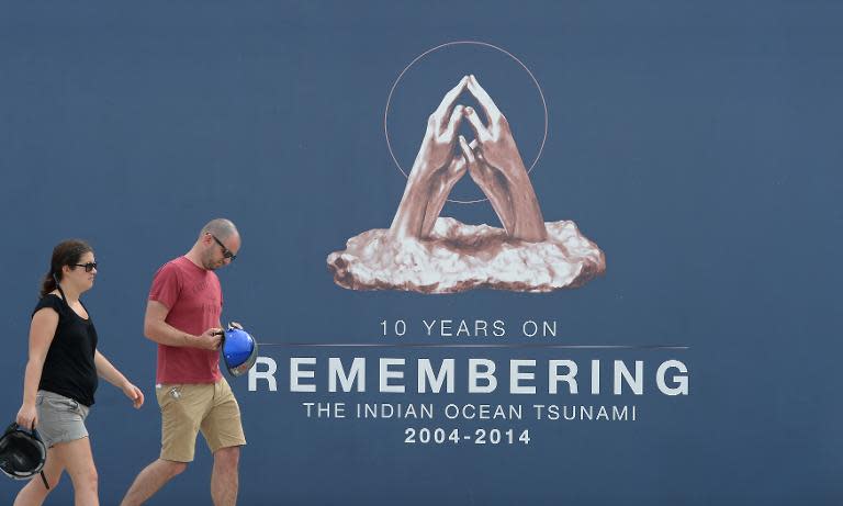 Tourists walk past a large poster for the 10th anniversary of the 2004 tsunami in Phang-nga province, Thailand