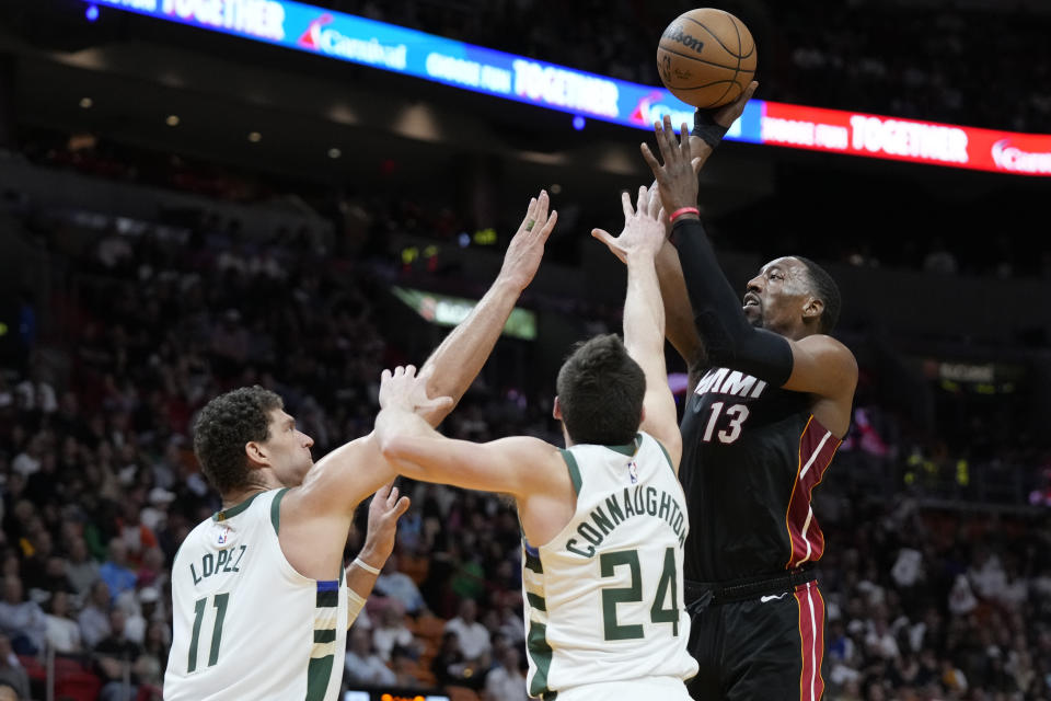 Miami Heat center Bam Adebayo (13) takes a shot against Milwaukee Bucks center Brook Lopez (11) and guard Pat Connaughton (24) during the first half of an NBA basketball game, Thursday, Jan. 12, 2023, in Miami. (AP Photo/Wilfredo Lee)