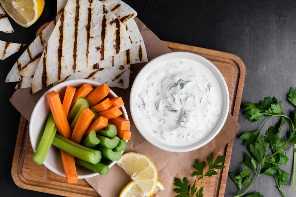 a bowl of tzatziki sauce and a bowl of carrots and celery with pita bread