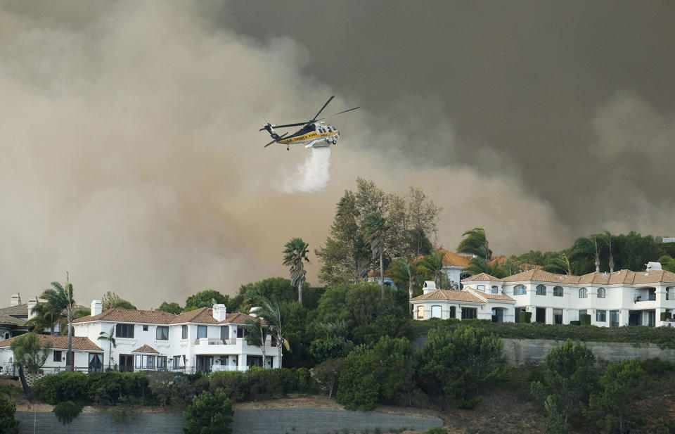 A helicopter drops water on a brush fire behind homes during the Woolsey Fire in Malibu on Friday. Souce: AP via AAP