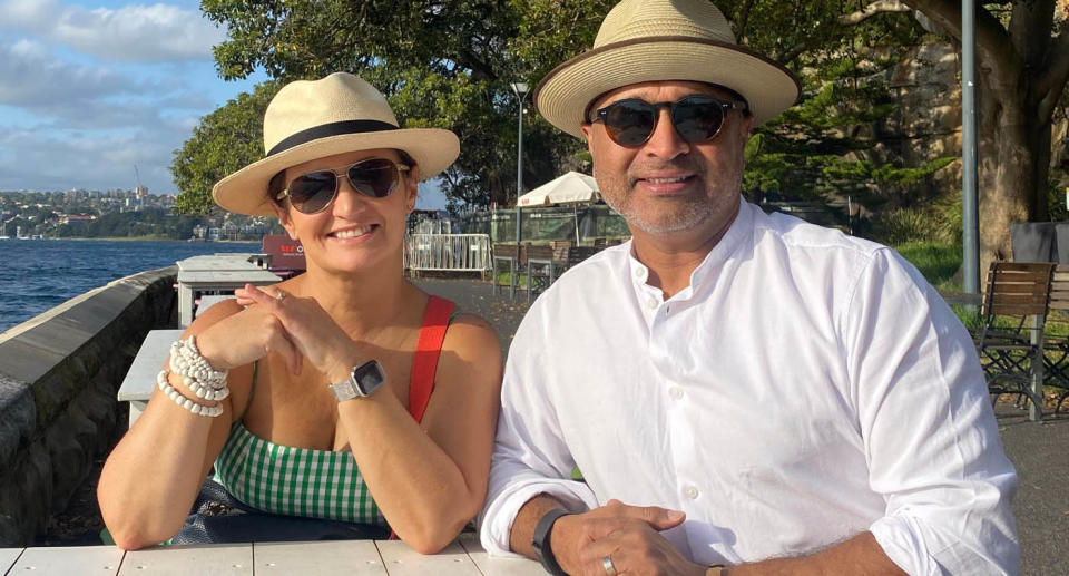 Sydney woman Margaret Khursigara and her husband sitting by water wearing hats. 