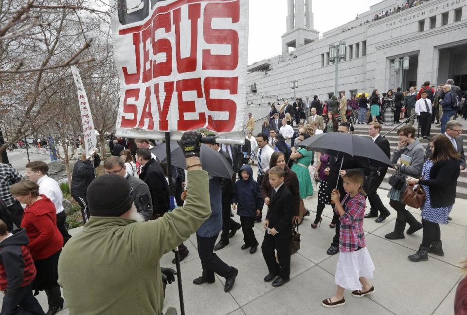 People walk pass a unidentified protester on their way from the Conference Center during opening session of the two-day Mormon church conference Saturday, April 5, 2014, in Salt Lake City. More than 100,000 Latter-day Saints are expected in Salt Lake City this weekend for the church's biannual general conference. Leaders of The Church of Jesus Christ of Latter-day Saints give carefully crafted speeches aimed at providing members with guidance and inspiration in five sessions that span Saturday and Sunday. They also make announcements about church statistics, new temples or initiatives. In addition to those filling up the 21,000-seat conference center during the sessions, thousands more listen or watch around the world in 95 languages on television, radio, satellite and Internet broadcasts. (AP Photo/Rick Bowmer)