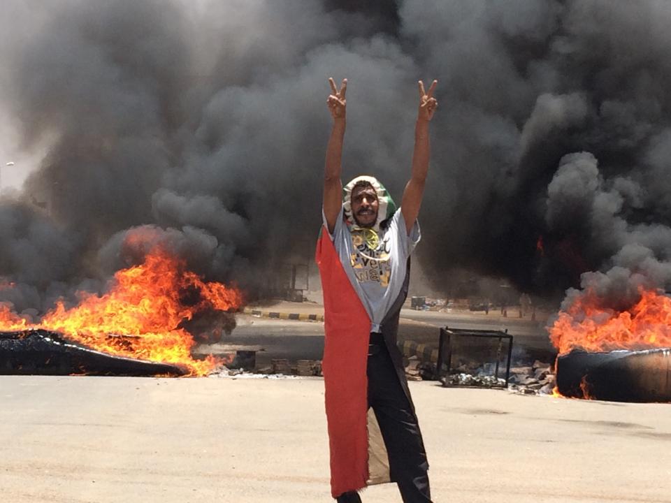 A protester flashes the victory sign in front of burning tires and debris on road 60, near Khartoum's army headquarters, in Khartoum, Sudan, Monday, June 3, 2019. Sudanese protest leaders say at least 13 people have been killed Monday in the military's assault on the sit-in outside the military headquarters in the capital, Khartoum. The protesters have announced they are suspending talks with the military regarding the creation of a transitional government. (AP Photo)