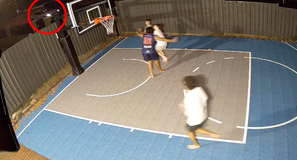 A backyard basketball court, believed to be at the home of Eddie Betts, has four boys playing together with a white car visible just beyond the fence. 