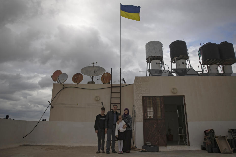 Ukrainian Oksana al-Astal stands with her Palestinian husband and their children as they pose for a photo as a Ukrainian flag waves over the roof top of their home in Khan Younis, southern Gaza Strip, Sunday, March 13, 2022. The al-Astal family is among dozens of Palestinian-Ukrainian families in the isolated territory who have experienced several wars firsthand — the most recent last May — and are now watching another unfold in Ukraine, where many of them have loved ones. (AP Photo/ Khalil Hamra)