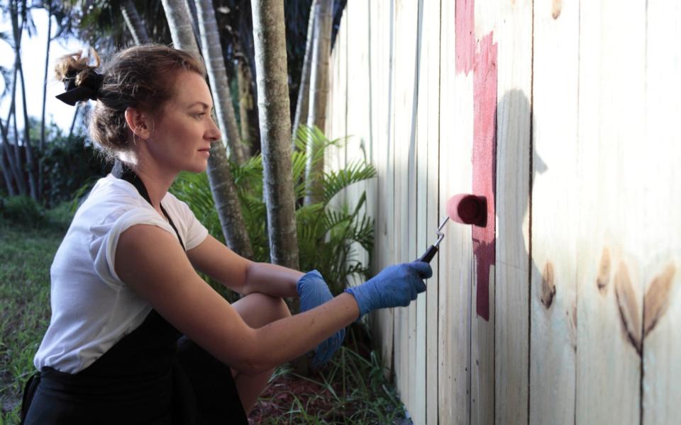 Young woman is painting a fence. - IStockPhoto