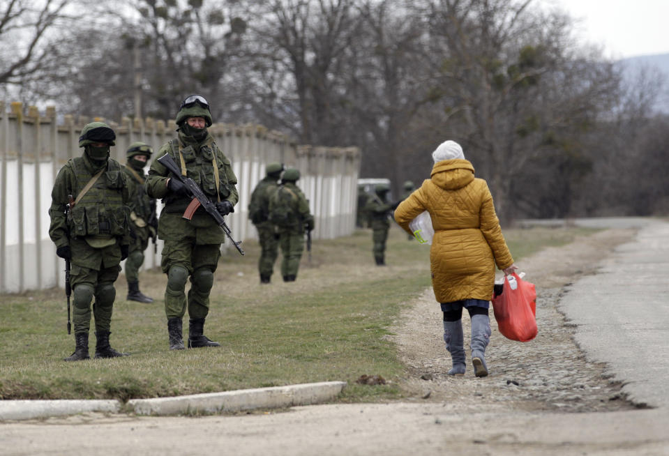 A woman passes by unidentified gunmen, as they guard Ukraine's infantry base in Privolnoye, Ukraine, Sunday, March 2, 2014. Hundreds of unidentified gunmen arrived outside Ukraine's infantry base in Privolnoye in its Crimea region. The convoy includes at least 13 troop vehicles each containing 30 soldiers and four armored vehicles with mounted machine guns. The vehicles — which have Russian license plates — have surrounded the base and are blocking Ukrainian soldiers from entering or leaving it. (AP Photo/Darko Vojinovic)