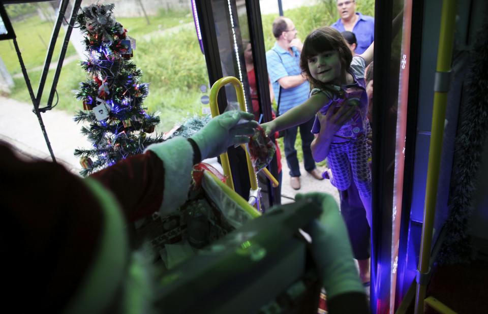 Bus driver Edilson, 45, also known as "Fumassa", gives sweets to a girl as he wears a Santa Claus outfit inside an urban bus decorated with Christmas motives in Santo Andre, outskirts of Sao Paulo, December 10, 2013. Fumassa dresses as Santa Claus every year while driving his bus. Picture taken December 10. REUTERS/Nacho Doce (BRAZIL - Tags: SOCIETY TRANSPORT)