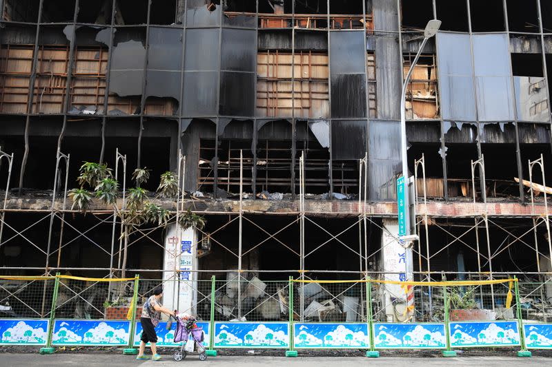 Person pushes a trolley past a residential building damaged after a fire, in Kaohsiung