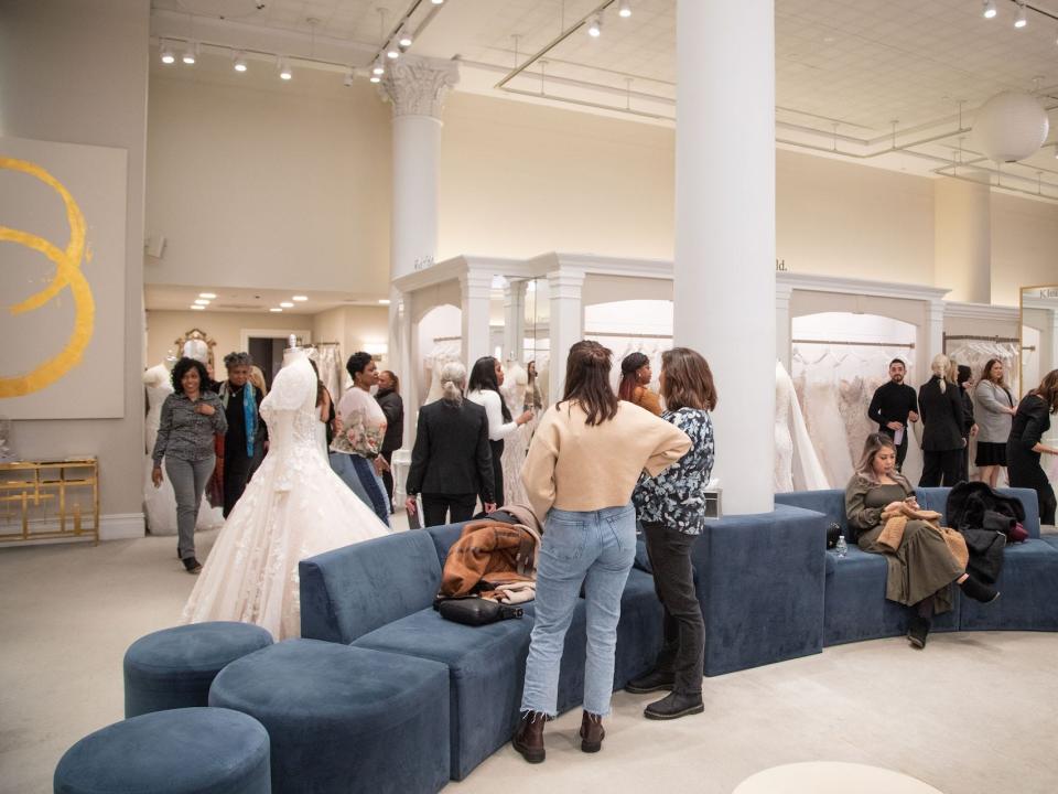 A large room with women walking around and wedding dresses.