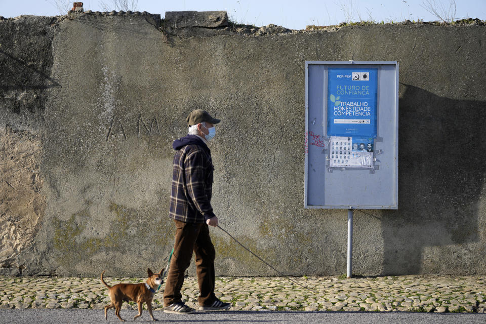A man walks past a Portuguese Communist Party election poster in the outskirts of Lisbon, Tuesday, Jan. 25, 2022. Portuguese voters go to the polls Sunday, two years earlier than scheduled after a political crisis over a blocked spending bill brought down the country's minority Socialist government and triggered a snap election. (AP Photo/Armando Franca)