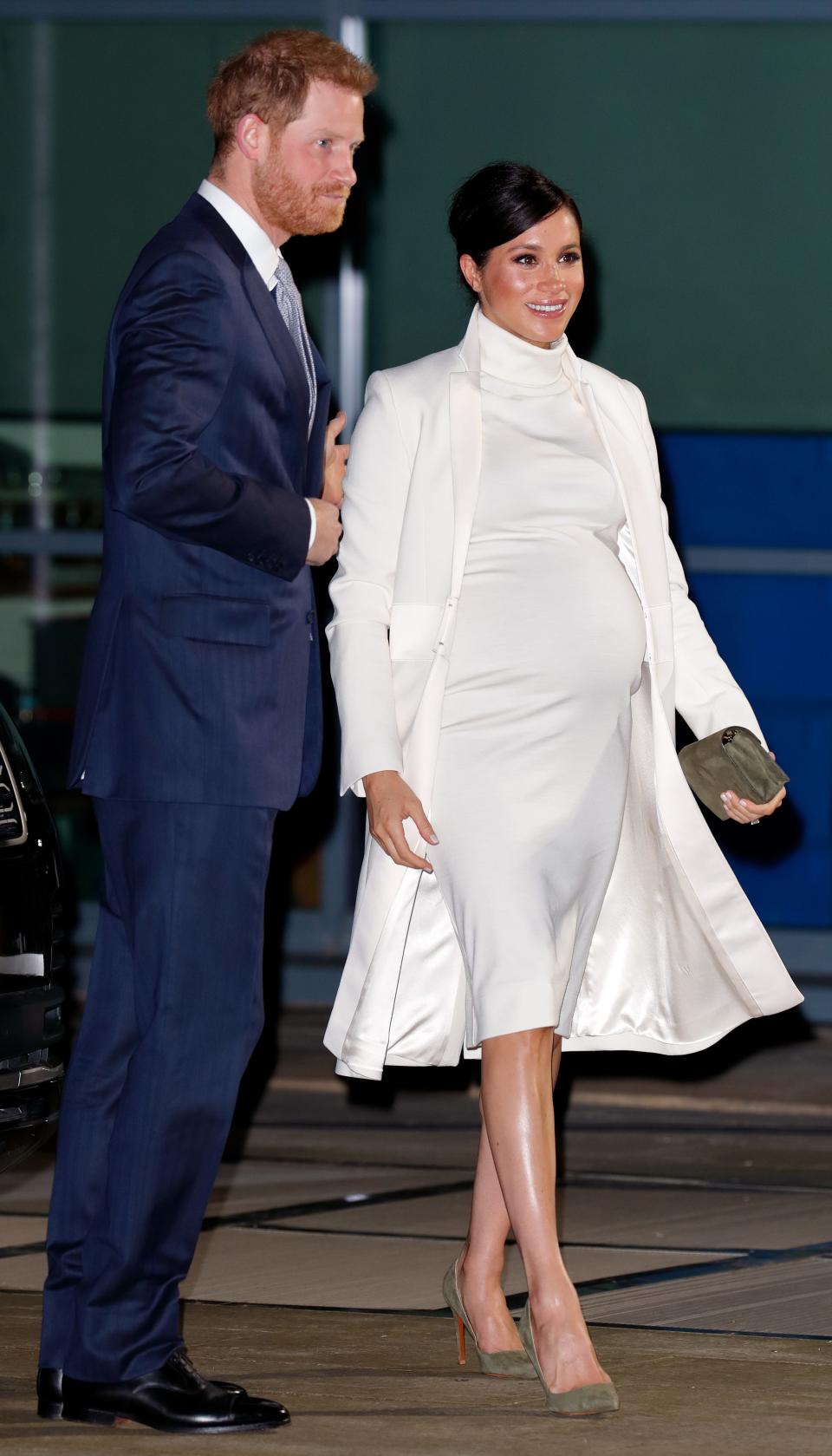Harry in a navy suit and Meghan pregnant in a snug white turtleneck knee length dress and matching flowy coat.