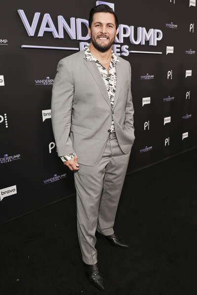 Brock Davies wearing a grey suit in front of a step and repeat.